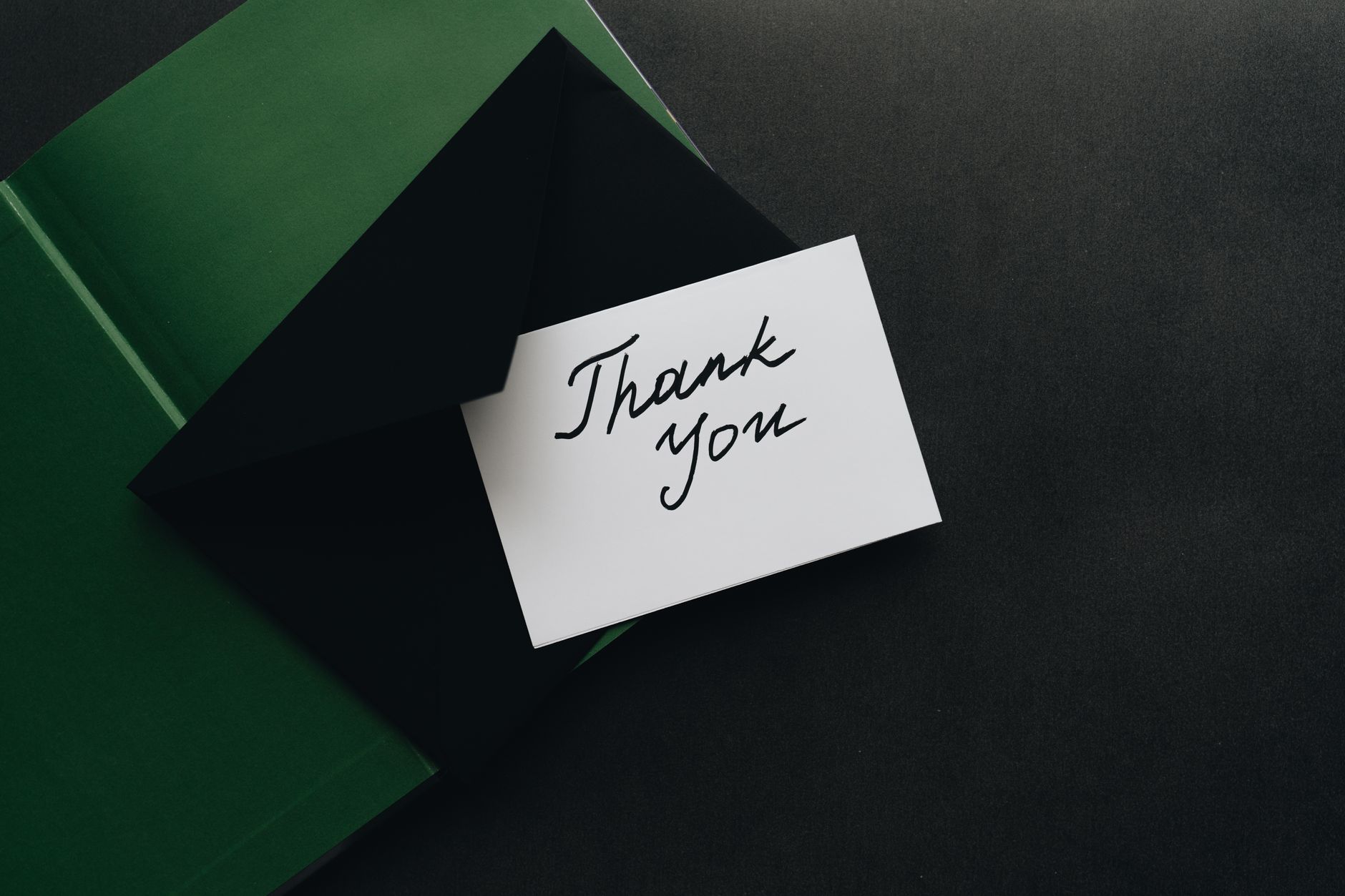 A handwritten thank-you card and envelope on a wooden table